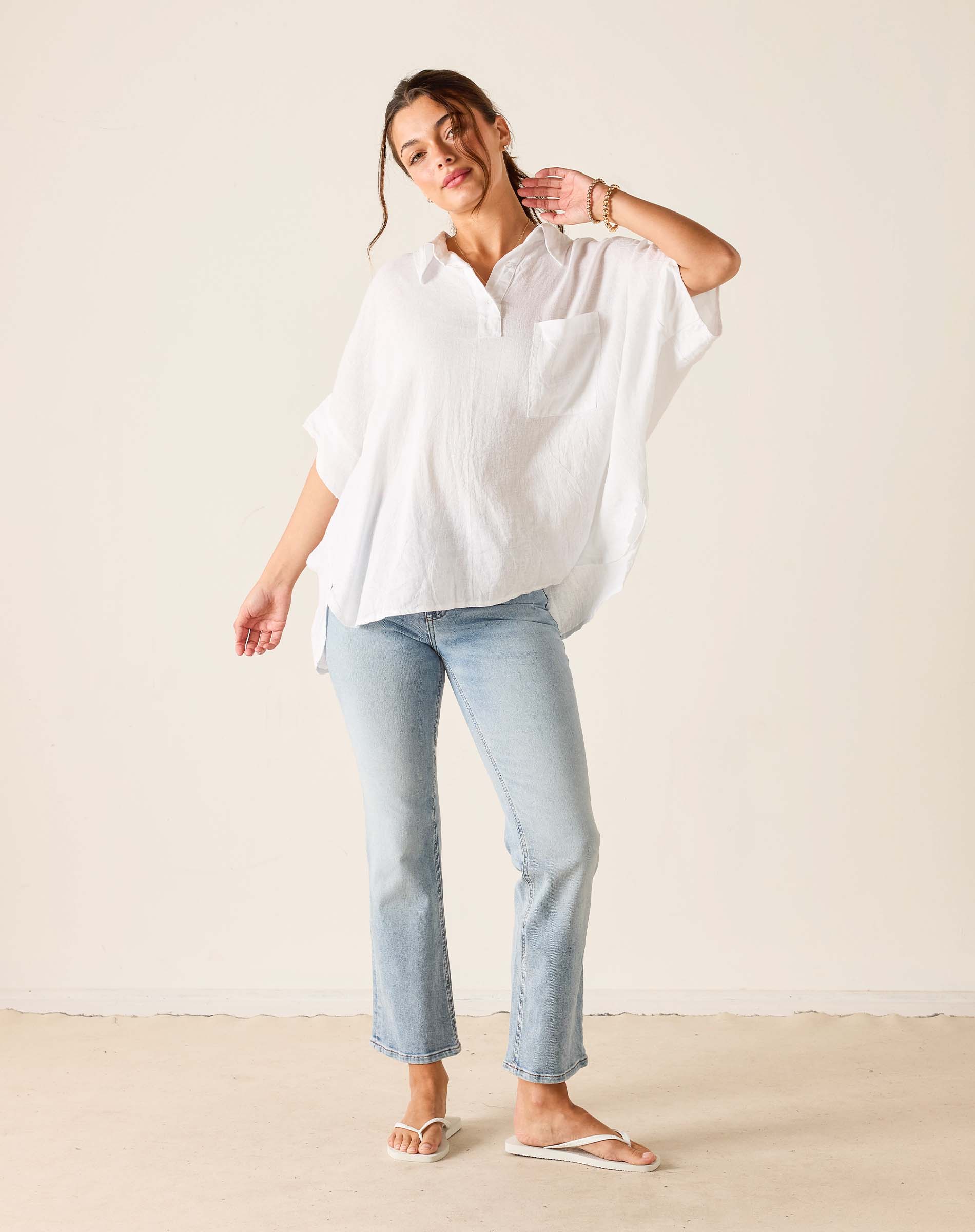 Woman wearing a white shirt and light blue jeans against a plain background