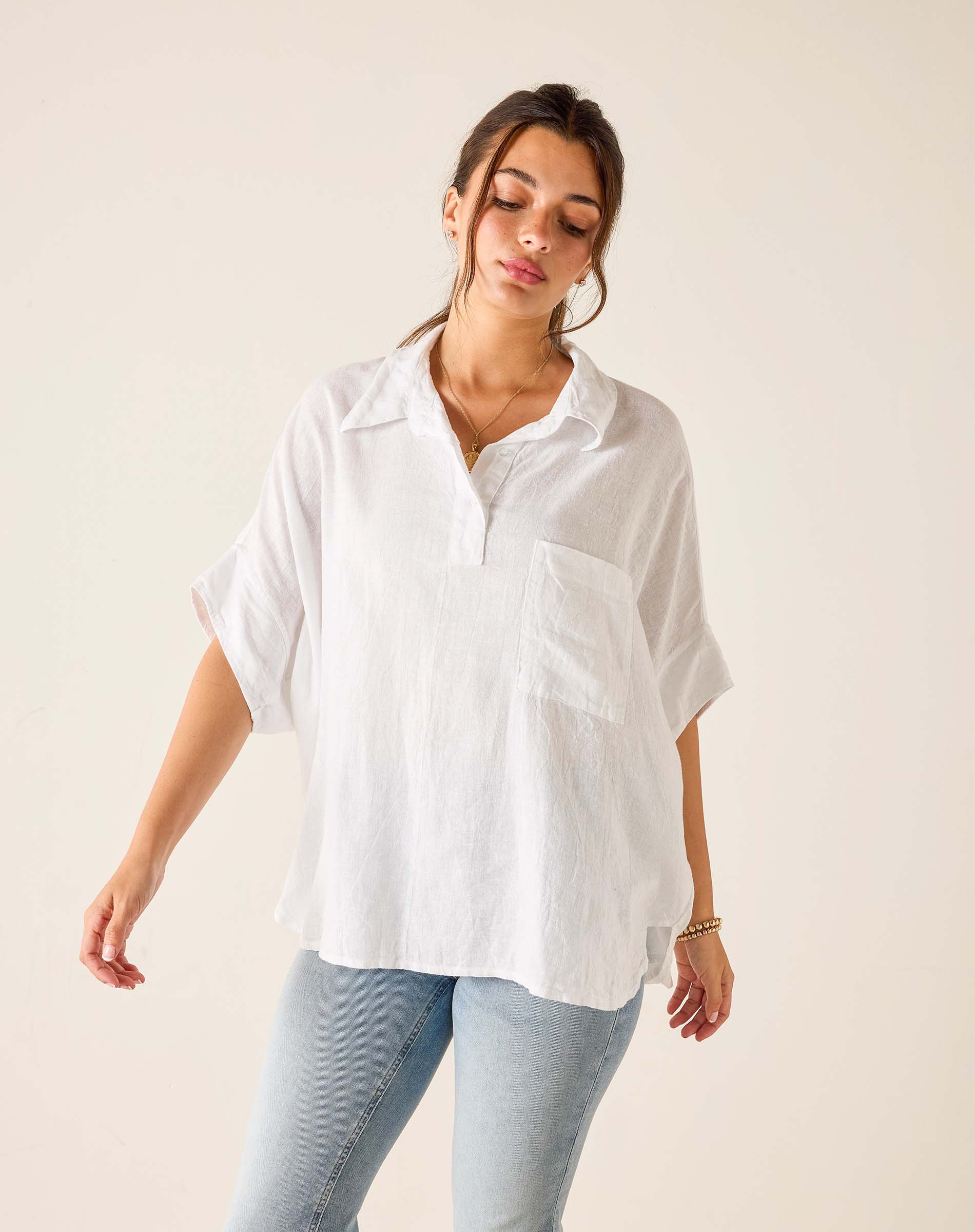 Woman wearing a white oversized shirt and light blue jeans against a plain background
