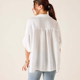 Woman wearing a white shirt and light blue jeans against a plain background