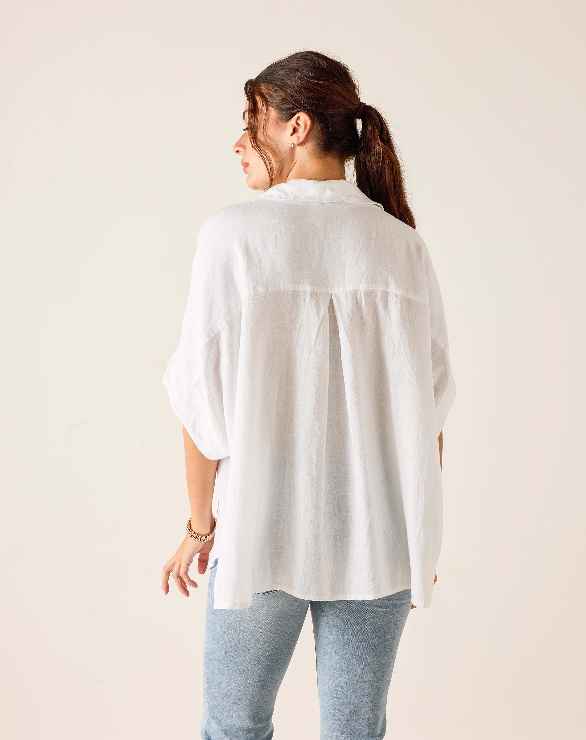 Woman wearing a white shirt and light blue jeans against a plain background