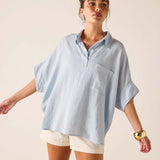 Woman wearing a light blue oversized shirt and white shorts on a beige background