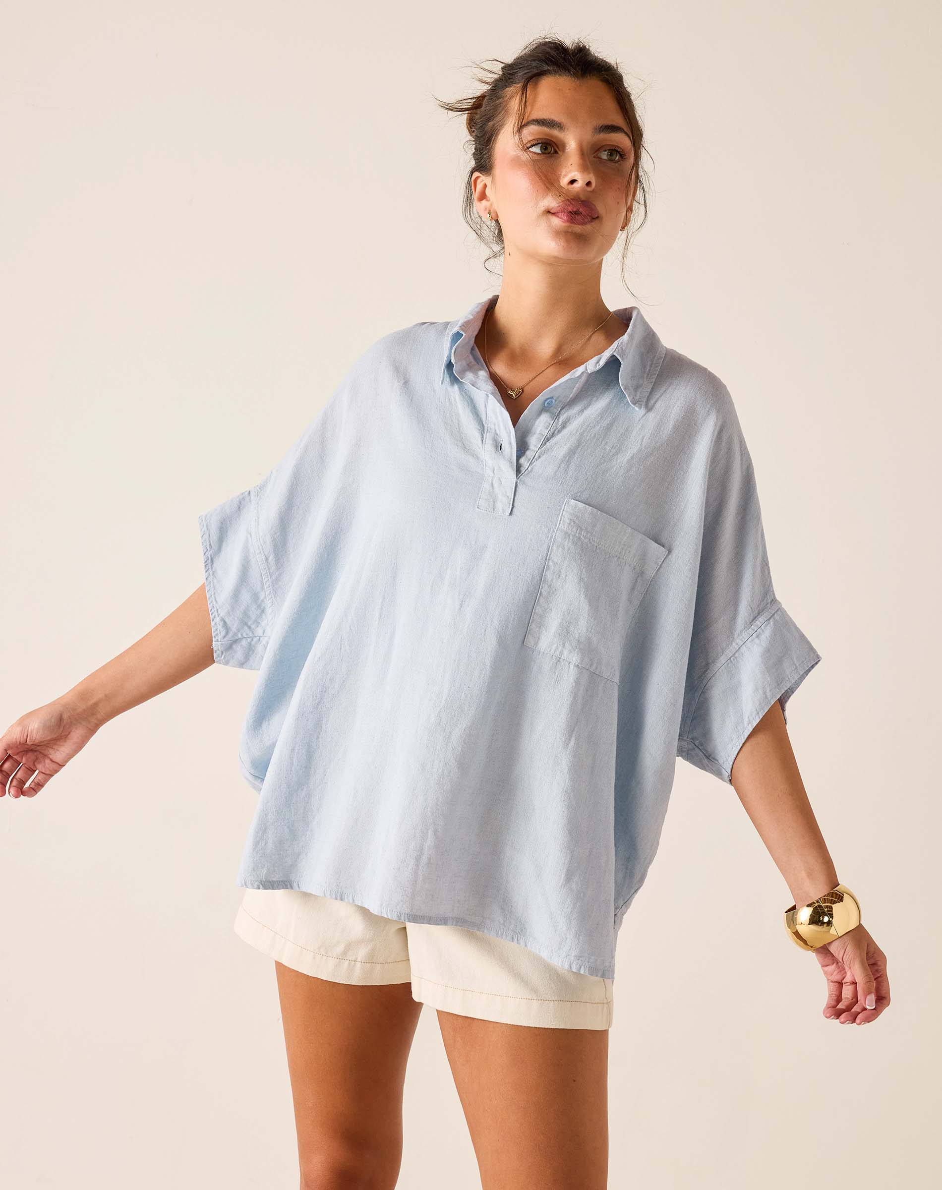 Woman wearing a light blue oversized shirt and white shorts on a beige background