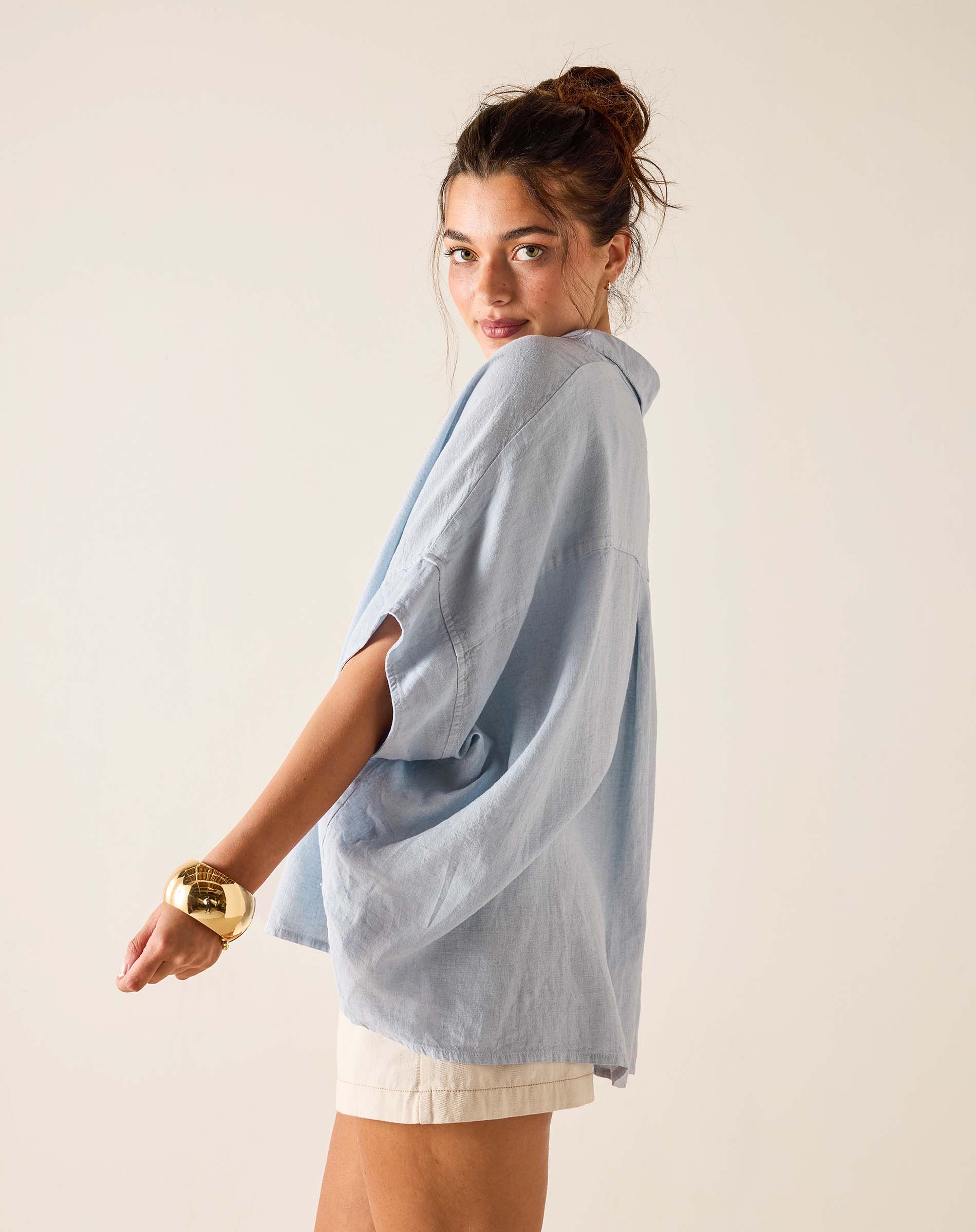Woman wearing a light blue oversized shirt against a plain background