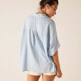Woman wearing a light blue oversized shirt and beige shorts on a plain background