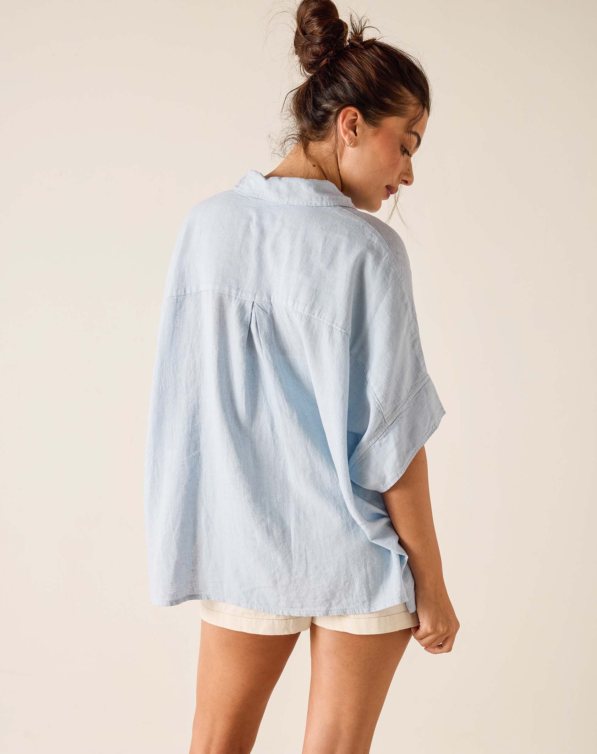 Woman wearing a light blue oversized shirt and beige shorts on a plain background