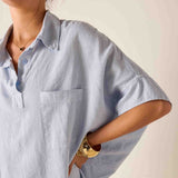 Person wearing a light blue oversized shirt with a neutral background