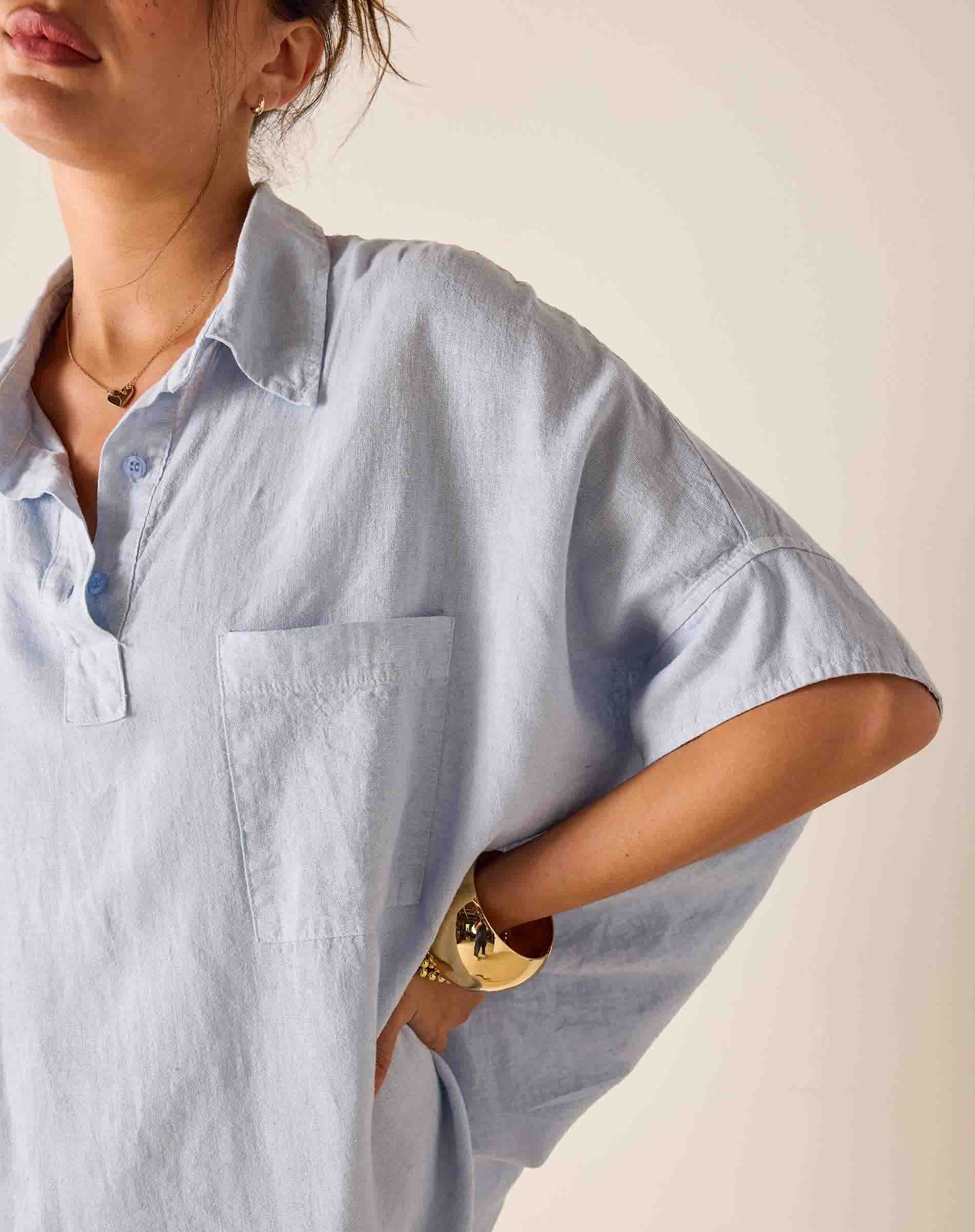 Person wearing a light blue oversized shirt with a neutral background