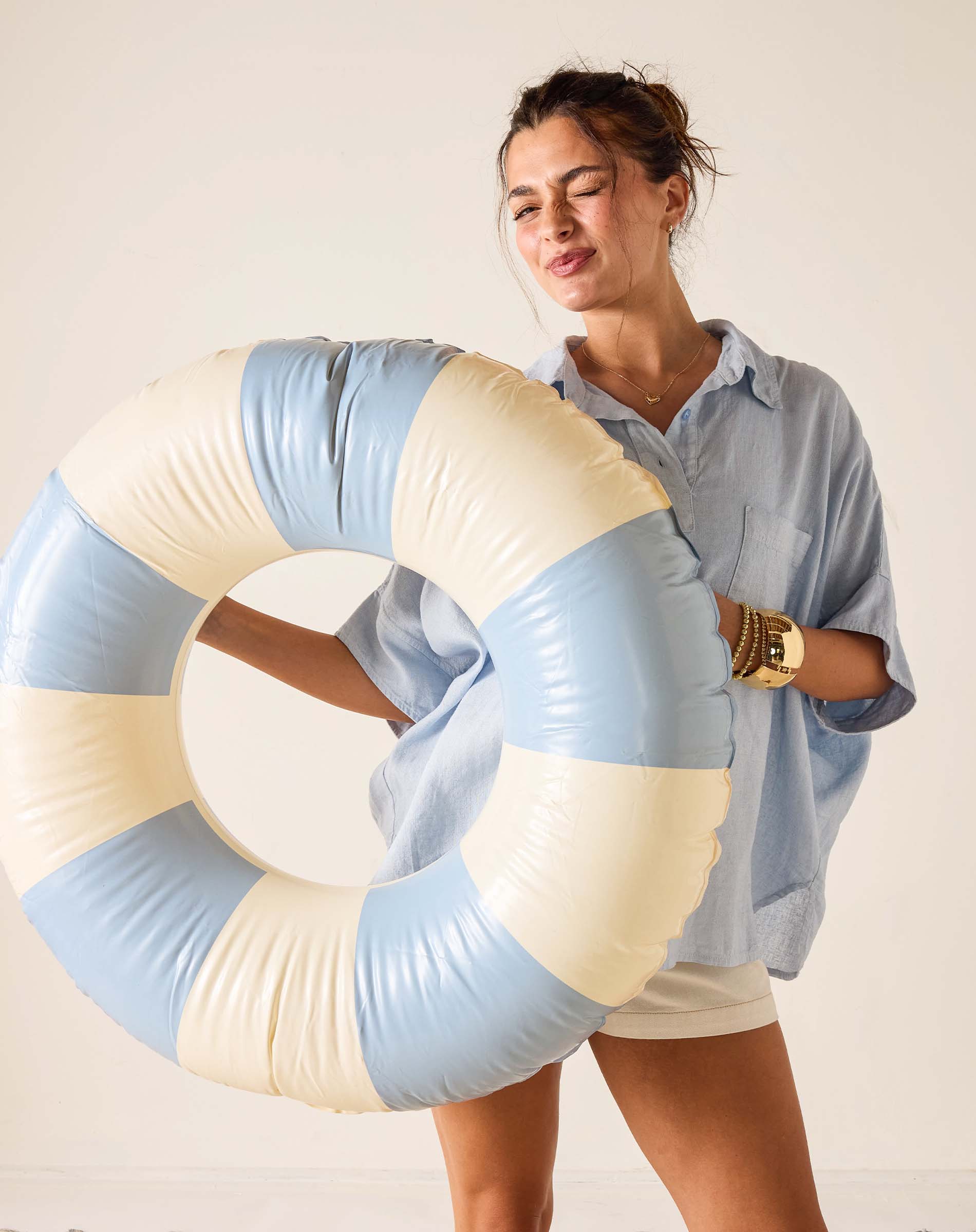 Woman holding a large inflatable ring with blue and beige colors against a plain background