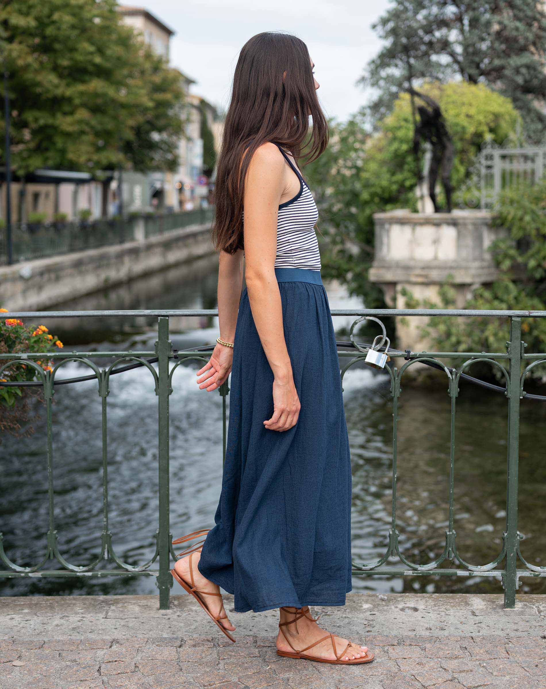 Woman standing by a canal with a bridge and greenery in the background