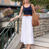 Woman standing on a stone staircase with a canal view, wearing a navy top and white skirt.