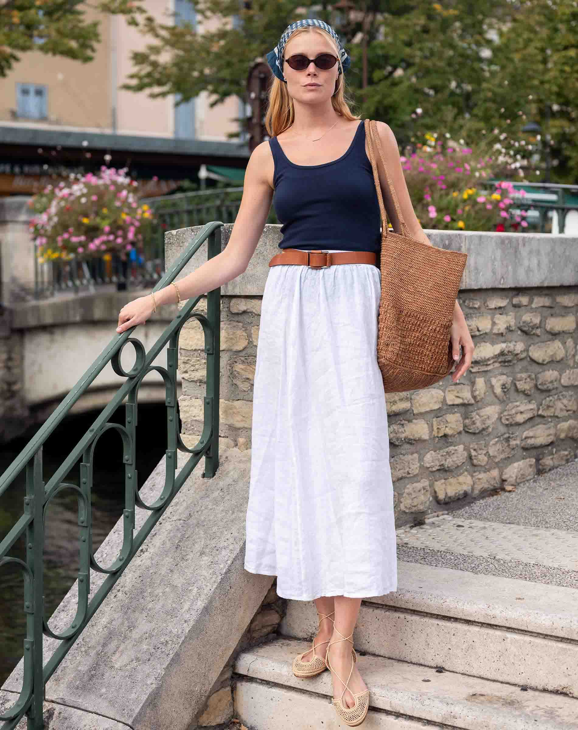 Woman standing on a stone staircase with a canal view, wearing a navy top and white skirt.