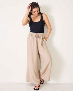 Woman wearing a black tank top and beige wide-leg pants against a white background