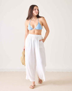 Woman wearing a blue bikini top and white pants against a white background