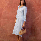 Woman in a light blue dress holding a woven bag against a textured red wall.