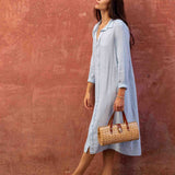 Woman in a light blue dress holding a woven bag against a red wall.