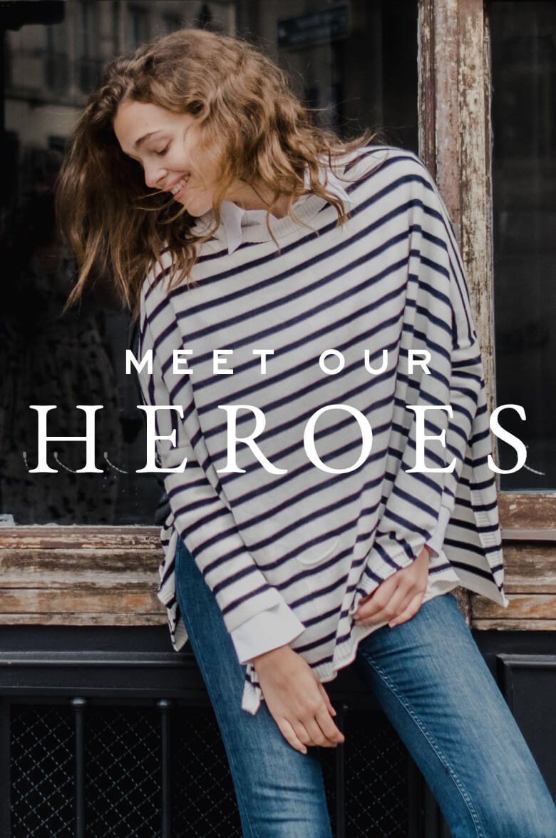 A woman in a striped knit sweater leaning against a window frame with text overlaying the image that reads: 'MEET OUR HEROES'