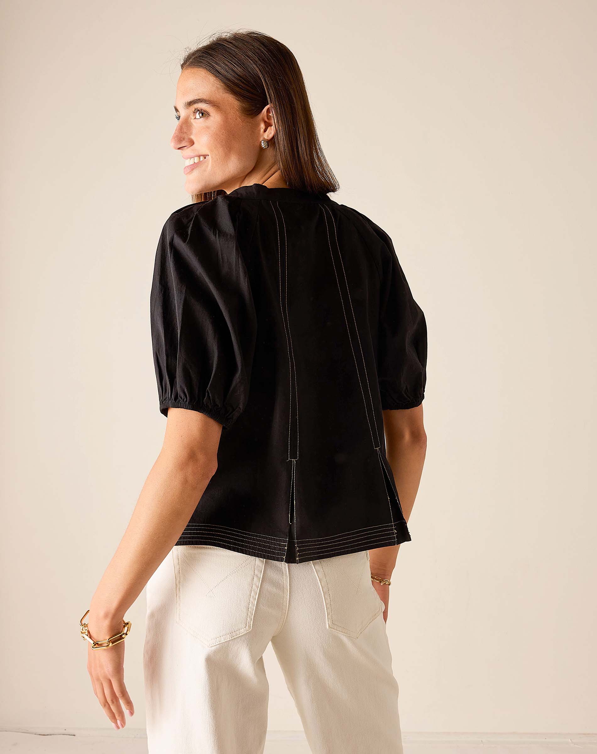 Back view of women's travel-friendly black puff-sleeve top with contrast stitching.