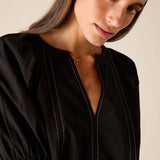 Black buttonless tunic top with vertical stitching and puffed sleeves.