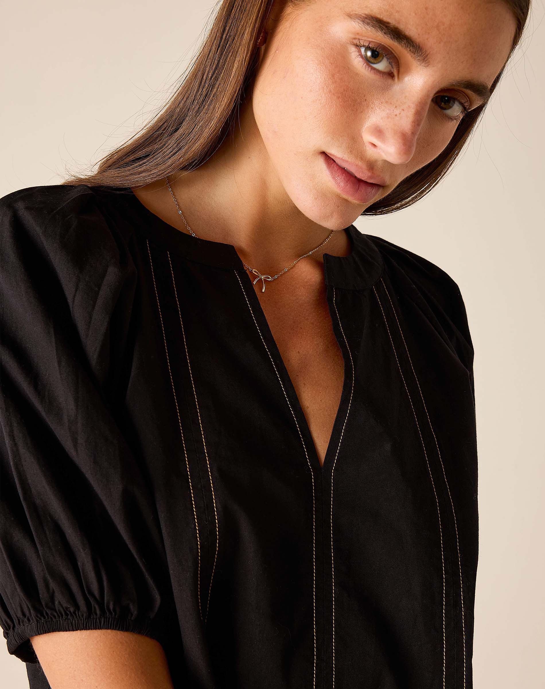 Black buttonless tunic top with vertical stitching and puffed sleeves.