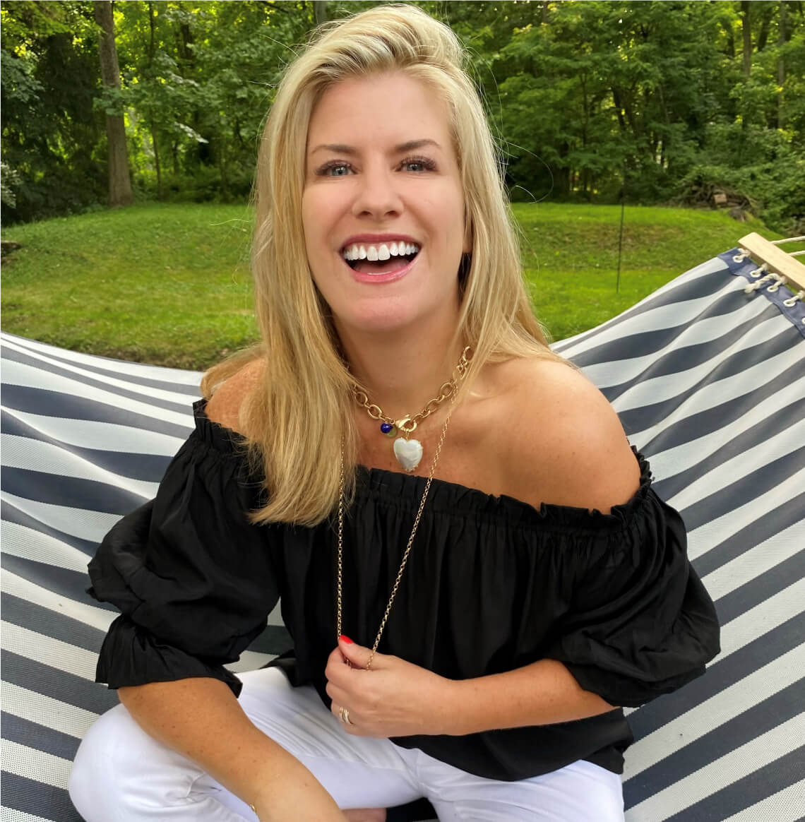Owner Jane Win wearing her necklaces and a MERSEA black tulum top with white jeans sitting on a hammock