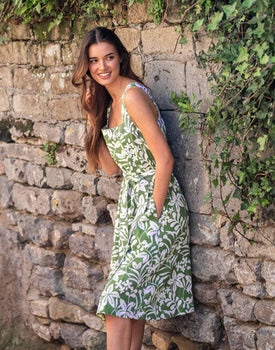 female wearing white and green floral A-line linen sundress with self-belt leaning on a stone wall