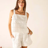 Woman wearing a white lace romper against a plain background