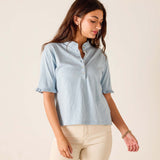 Woman wearing a light blue shirt and beige pants against a plain background