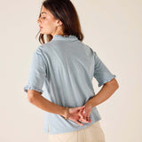 Woman wearing a light blue blouse with ruffled details on a beige background