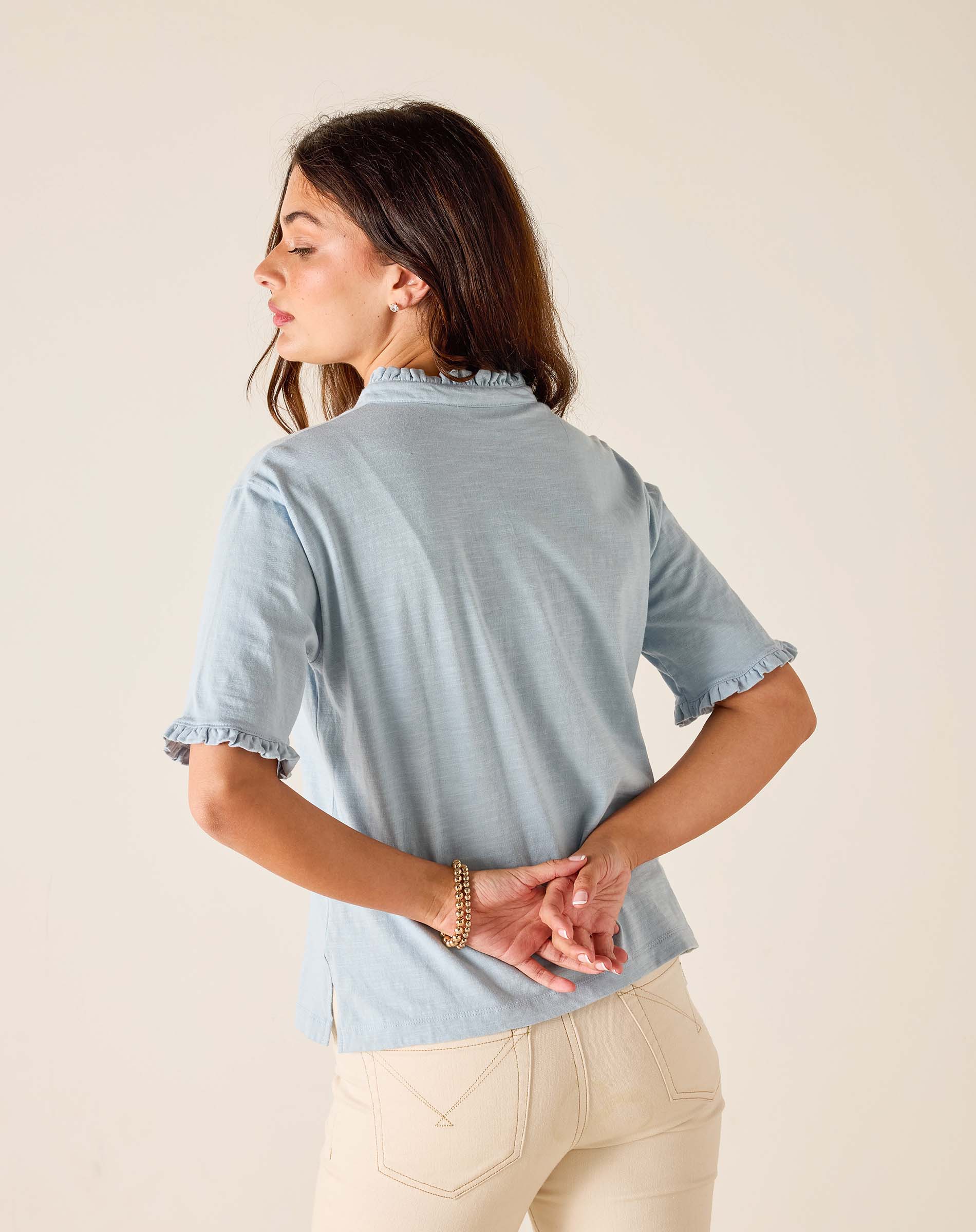 Woman wearing a light blue blouse with ruffled details on a beige background