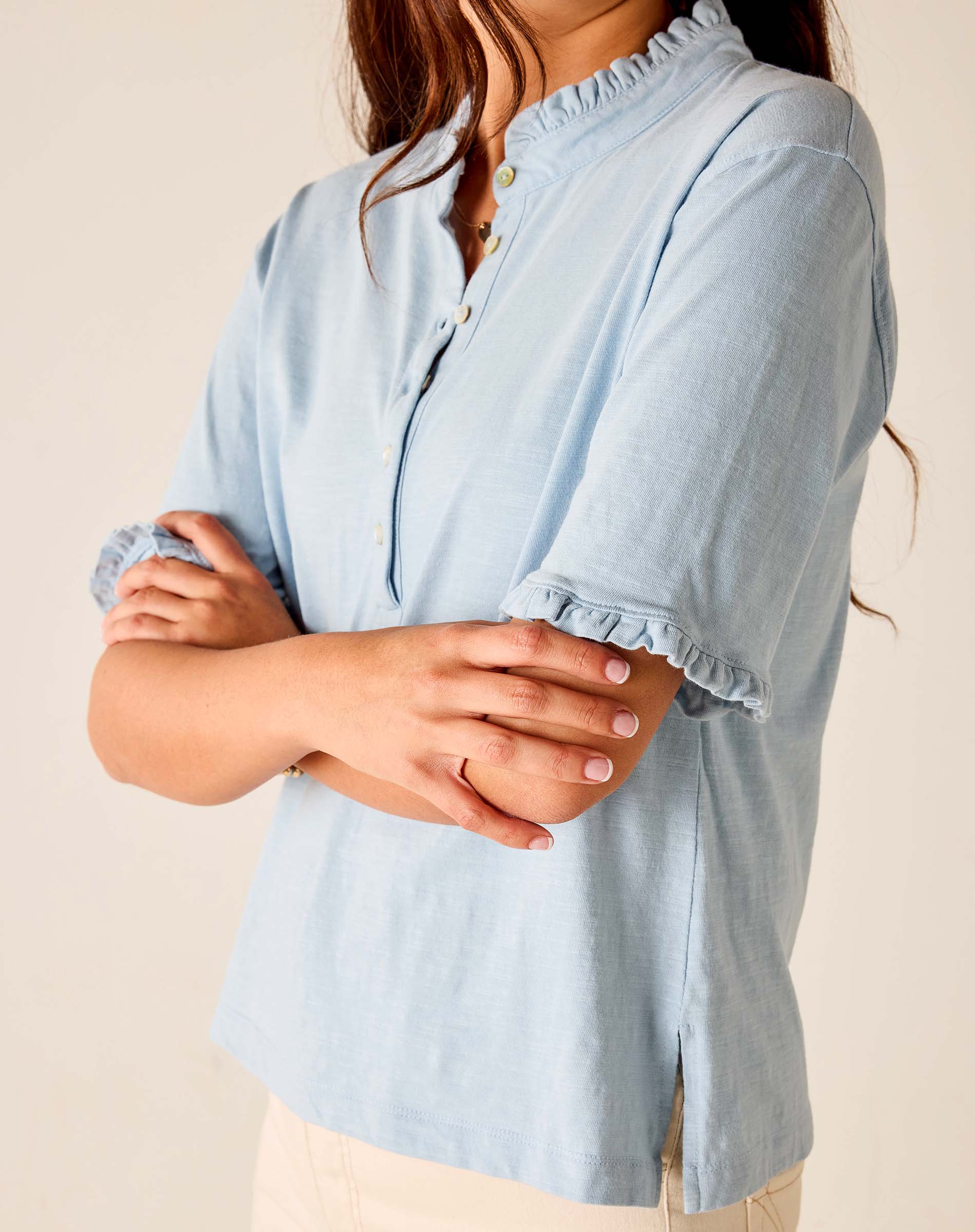 Light blue blouse worn by a person with arms crossed on a beige background