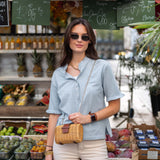 Woman standing in front of a market stall with produce and signs.