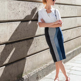 Woman in a white blouse and blue skirt standing against a concrete wall.