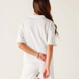 Woman wearing a white outfit with ruffled sleeves and shorts on a plain background