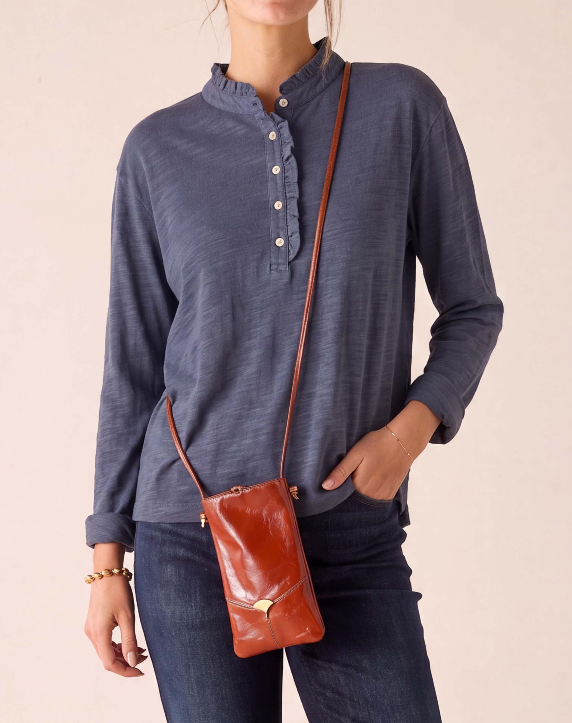MERSEA ladies' travel-ready dusty blue long sleeve ruffle henley top with a buttoned placket and denim pants.