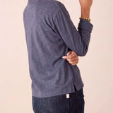 Side view of the woman wearing a women's travel-friendly dusty blue long-sleeve ruffle henley top and dark denim jeans.