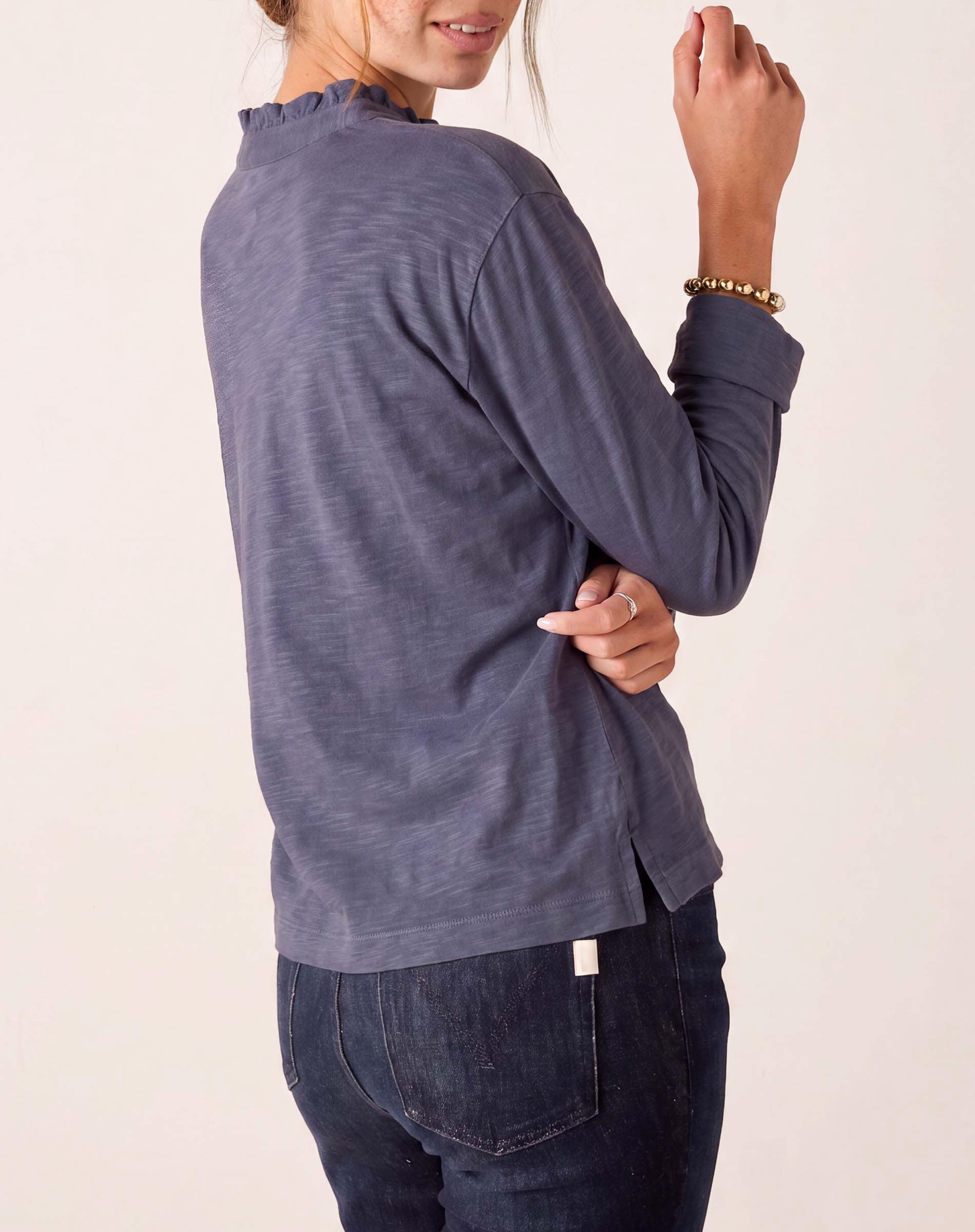 Dusty blue long sleeve ruffle henley knit top with a side view of the model wearing dark denim jeans