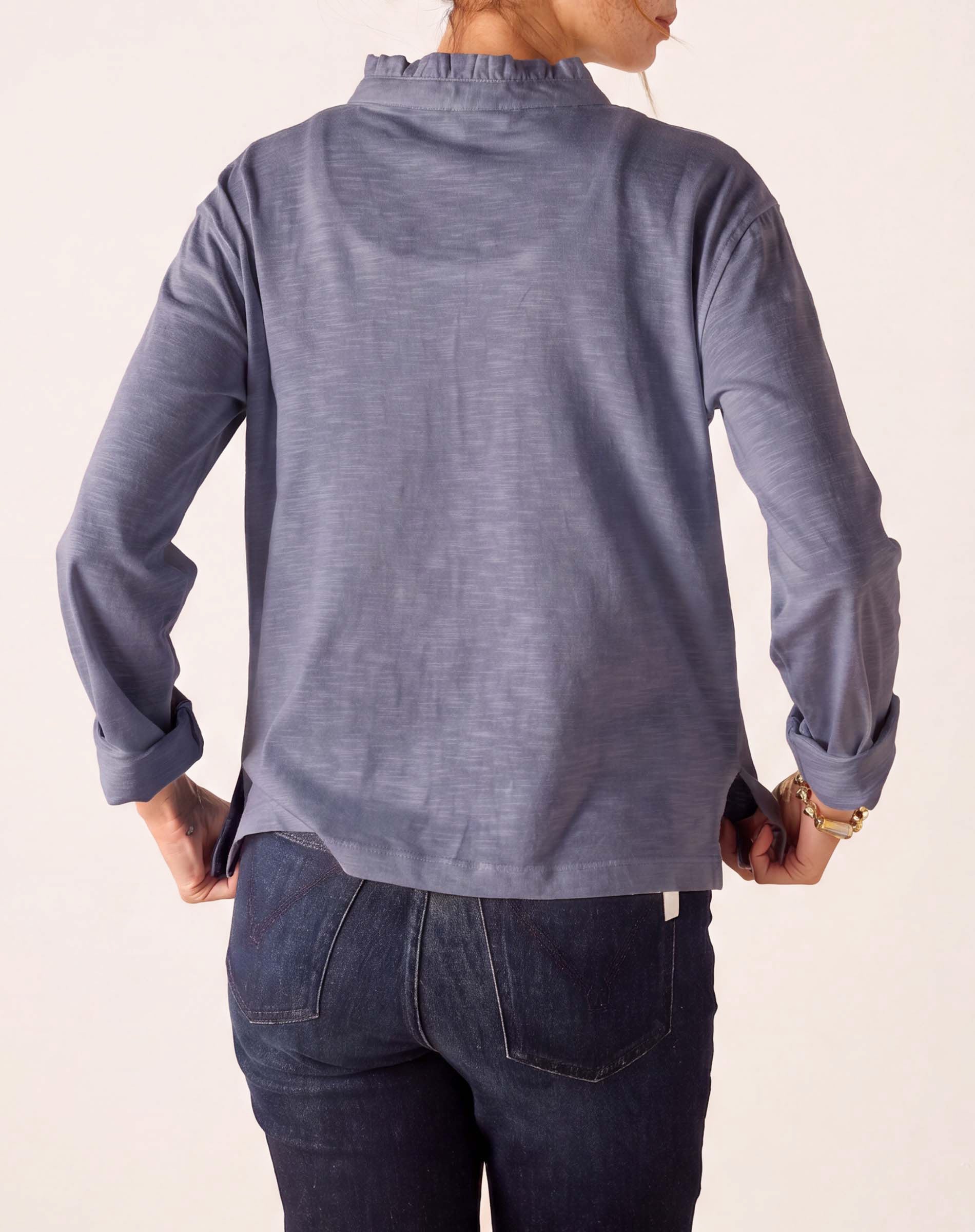 Back view of women's travel-friendly blue ruffled henley top with long sleeves and high-neck detail.