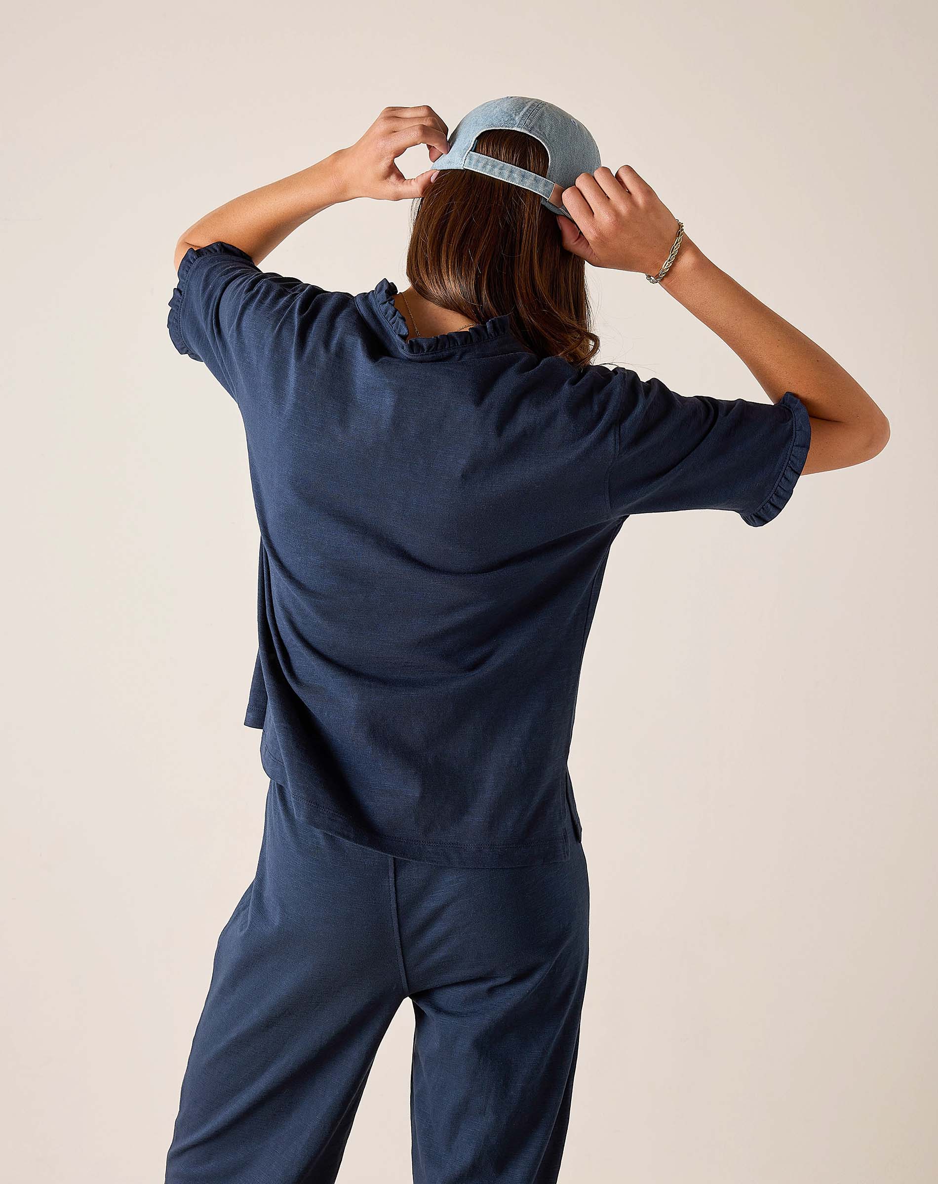 Person wearing a navy blue outfit with a cap on a beige background