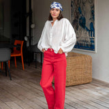 Woman wearing a white blouse and red pants in a room with a poster on the wall.