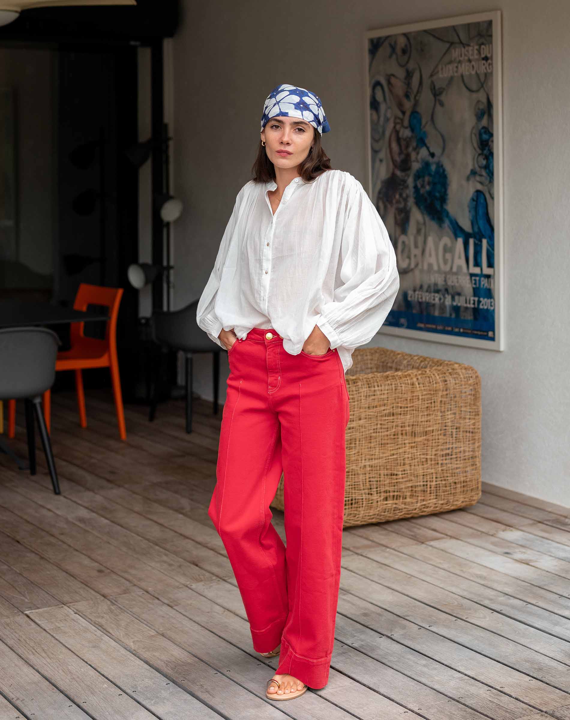 Woman wearing a white blouse and red pants in a room with a poster on the wall.