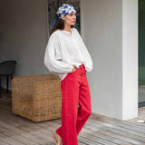 Woman wearing a white blouse and red pants with a blue patterned headscarf, standing on a wooden deck.