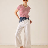 Woman wearing a red and white striped shirt, white pants, and sunglasses against a plain background