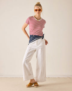 Woman wearing a red and white striped shirt, white pants, and sunglasses against a plain background