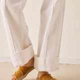 Person wearing white pants and brown sandals on a neutral background