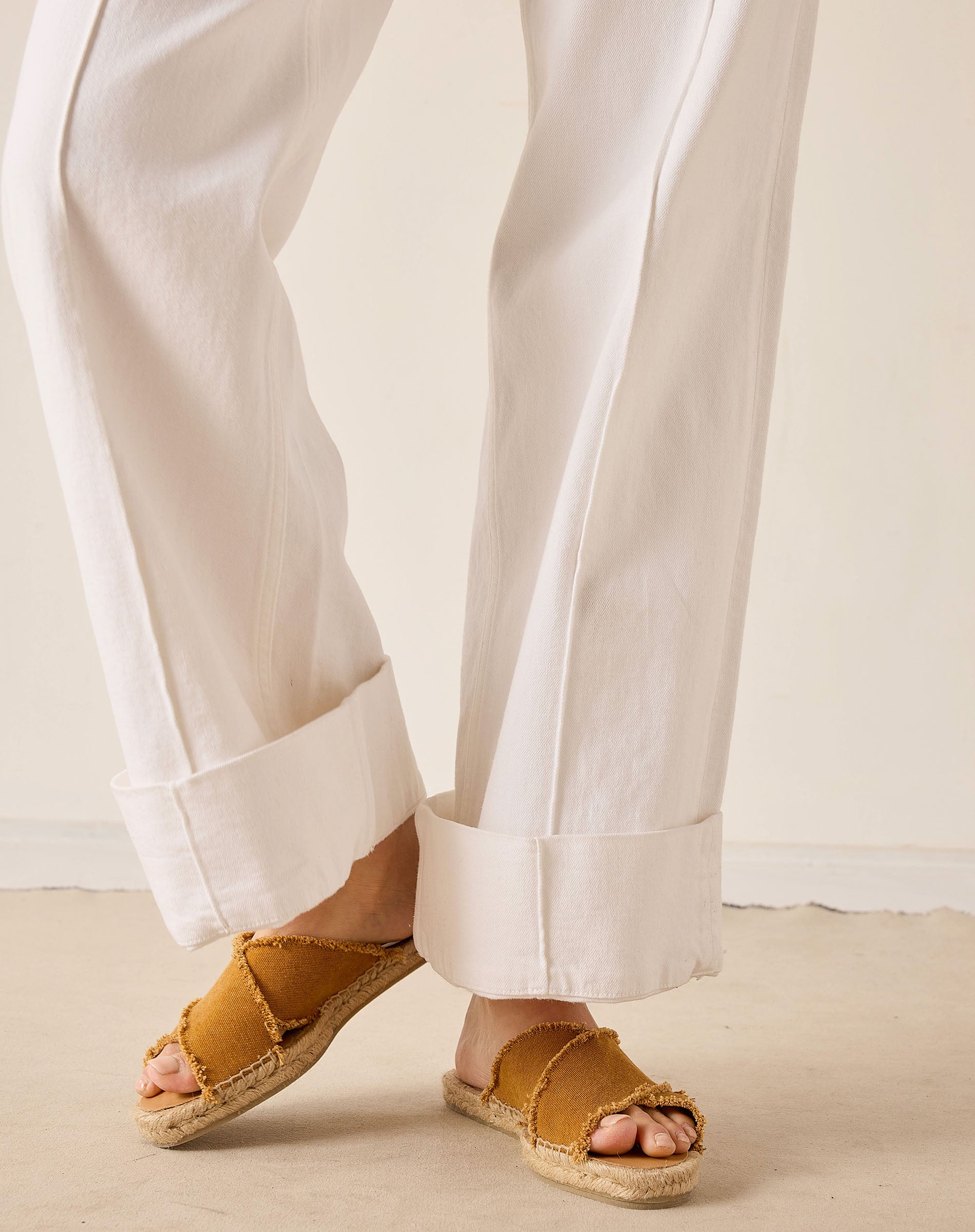 Person wearing white pants and brown sandals on a neutral background