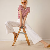 Woman sitting on a wooden stool wearing a red and white striped shirt and white pants.