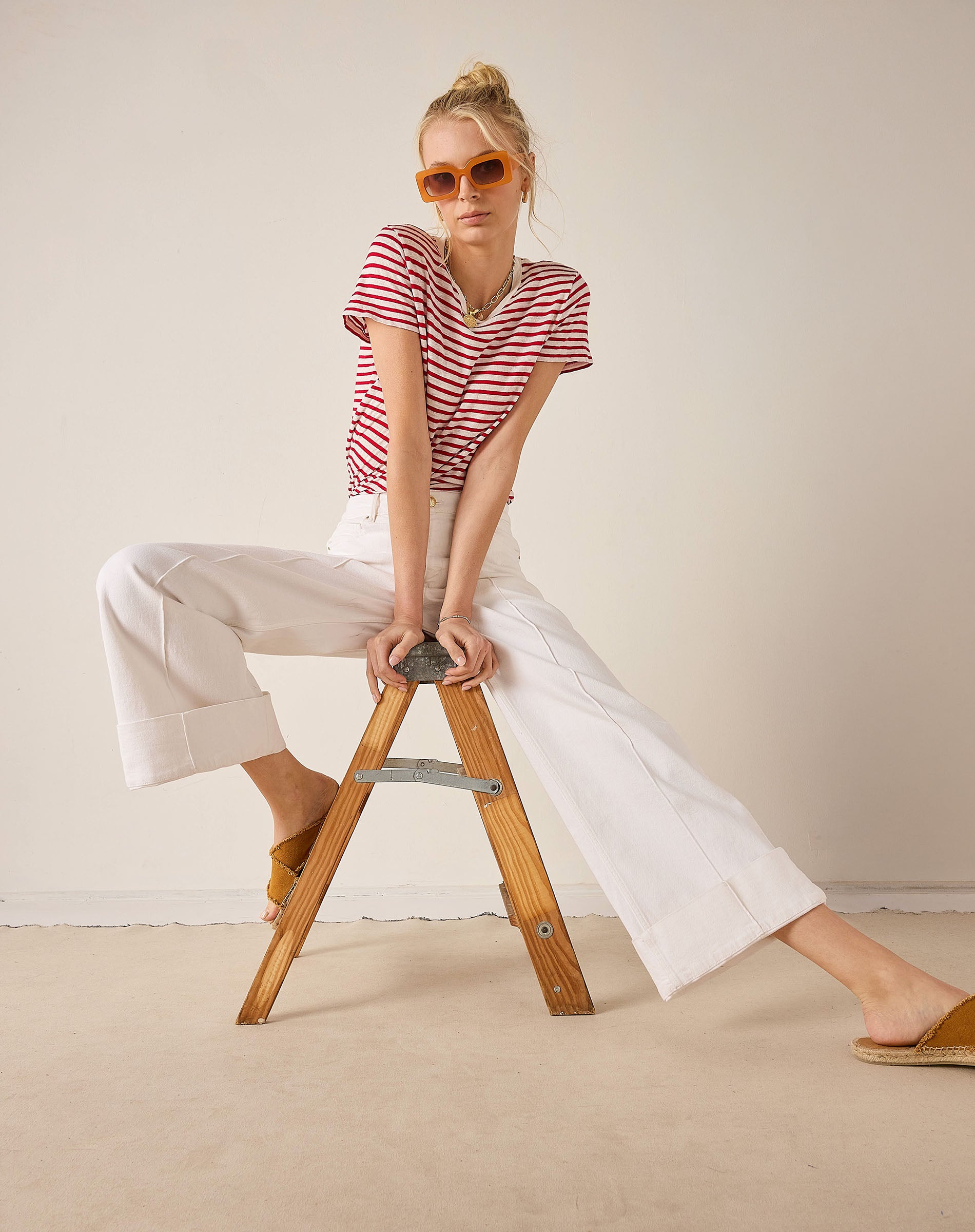 Woman sitting on a wooden stool wearing a red and white striped shirt and white pants.