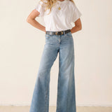 Woman wearing a white t-shirt and blue jeans against a plain background