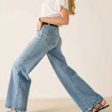 Person wearing light blue jeans and a white top on a plain background