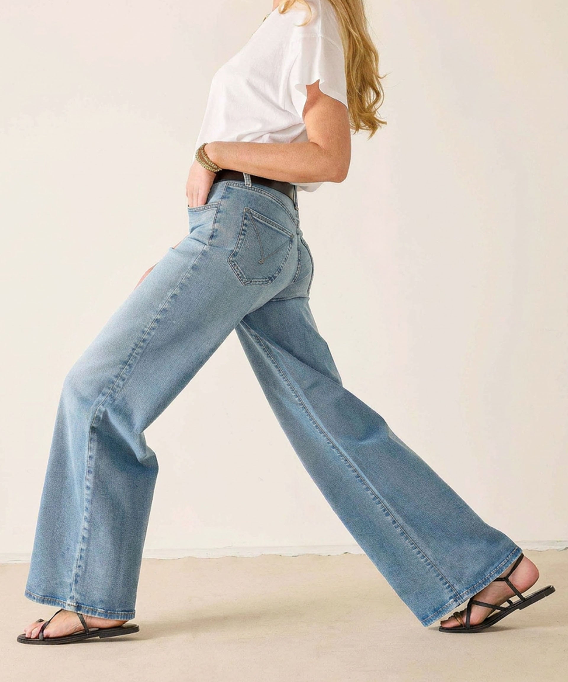Person wearing light blue jeans and a white top on a plain background